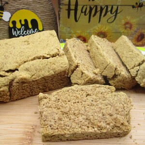 May include: A close-up of a wooden cutting board with several slices of light brown bread. The bread is arranged in a row, with the largest slice at the front. The bread has a slightly rough texture and a light brown color. The cutting board is made of wood and has a light brown color.