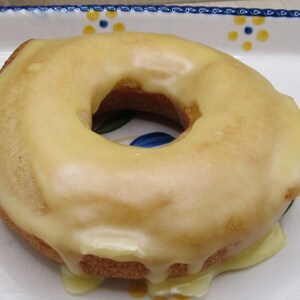 May include: A glazed donut with a light brown base and a thick, creamy yellow glaze. The glaze is dripping down the sides of the donut. The donut is on a decorative white plate with colorful floral patterns.