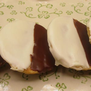 May include: Four black and white cookies arranged on a decorative plate with a green floral pattern. Each cookie is half covered in white icing and half in dark chocolate icing.