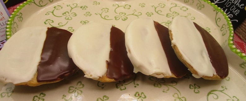 May include: Four black and white cookies arranged on a decorative plate with a green floral pattern. Each cookie is half covered in white icing and half in dark chocolate icing.