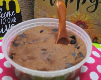 May include: A clear plastic container filled with chocolate chip cookie dough, a wooden spoon is partially inserted into the dough.