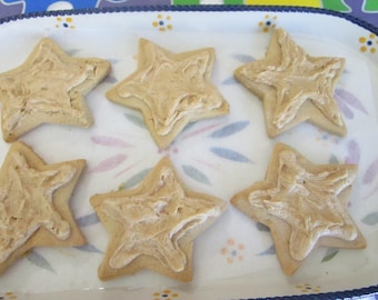 May include: Six star-shaped cookies with light brown frosting on a white and floral patterned serving dish. The cookies are arranged on a piece of parchment paper.