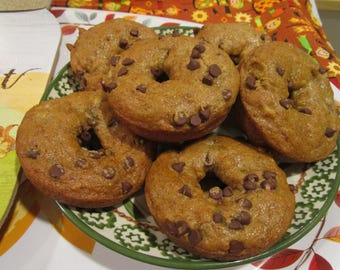 May include: A stack of golden-brown baked ring-shaped cakes topped with dark chocolate chips. The cakes are arranged on a round plate with a green rim and a decorative pattern, featuring a textured surface and a soft, porous crumb appearance.