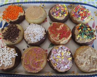 May include: A rectangular ceramic tray with a blue scalloped edge and floral pattern holds twelve round cookies. Each cookie is topped with light brown frosting and various decorations, including orange, chocolate, white, red, and multi-colored sprinkles.