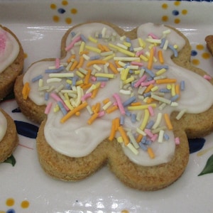 May include: Three decorated cookies in the shape of a butterfly, flower, and tulip. The butterfly cookie has pink sprinkles, the flower cookie has colorful sprinkles, and the tulip cookie has yellow sprinkles. All cookies have white icing.