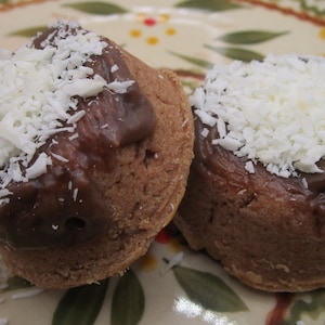 May include: Two chocolate cupcakes with dark chocolate frosting and a generous topping of shredded coconut. The cupcakes are on a decorative plate with a floral design.