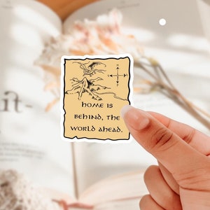 May include: A sticker with a hand-drawn map of a mountain range and a dragon flying overhead. The map has a compass and the text "home is behind, the world ahead."