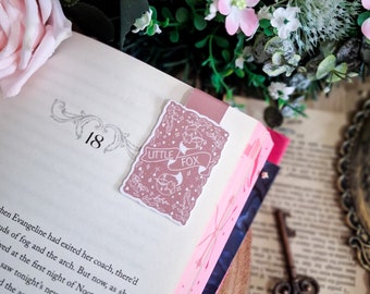 May include: A pink and white book with the text "Little Fox" on a pink and white bookmark. The book is open to page 18 and the bookmark is on the page.