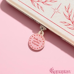 May include: A white zipped pouch featuring red line art of leaves and stars. A circular zip pull charm displays the red text "books are my love language" surrounded by a border of small red hearts. The brand name Romantasy Designs is visible.