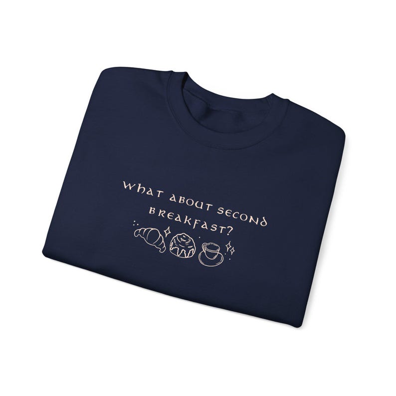 May include: Navy blue t-shirt with the text "What about second breakfast?" in white with a graphic of a croissant, a pastry, and a cup of coffee.