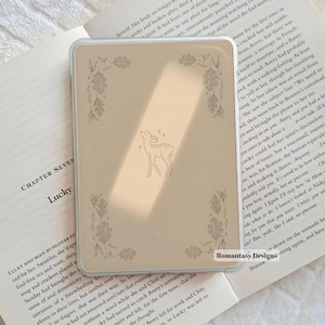 May include: A rectangular, clear e-reader case featuring a beige insert with a central line-art illustration of a small deer surrounded by four corner clusters of oak leaves and small stars. The text Romantasy Designs is printed in the bottom right.