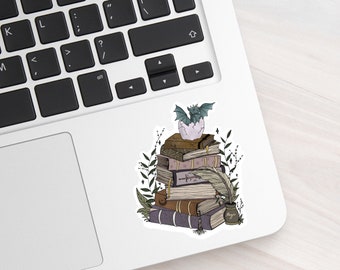 May include: A stack of old, leather-bound books with a small, gray dragon emerging from an egg on top. The books are surrounded by green leaves and a quill pen is resting on top of the stack. A small, brown bottle with the word "Magic" on it is at the bottom of the stack.