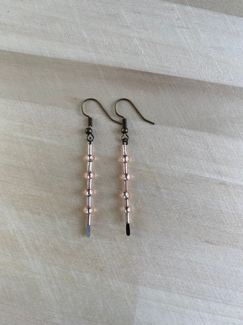 Pu&ograve; includere: Un paio di orecchini pendenti con finitura argentata. Ogni orecchino presenta una serie di piccole perle rotonde color pesca.