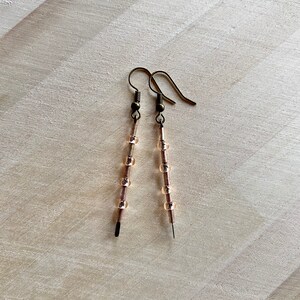 Pu&ograve; includere: Un paio di orecchini lunghi e delicati con un filo di bronzo e piccole perline di vetro trasparenti.