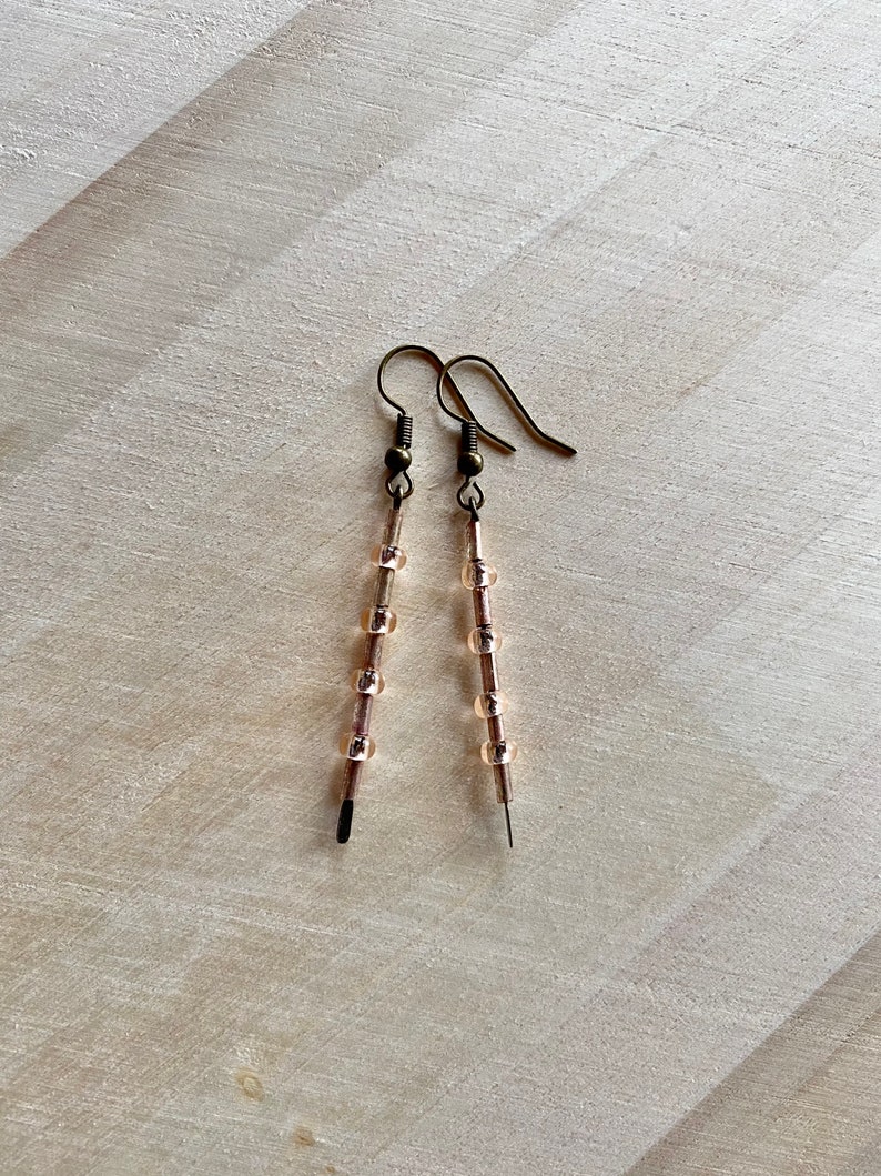 Pu&ograve; includere: Un paio di orecchini lunghi e delicati con un filo di bronzo e piccole perline di vetro trasparenti.