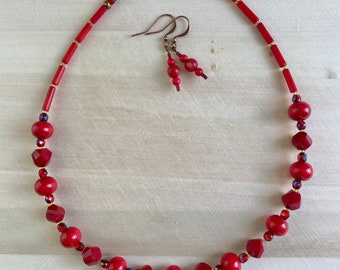 May include: A red beaded necklace and matching earrings set. The necklace features a variety of red beads, including round and faceted shapes, interspersed with smaller gold-colored beads. The earrings have a similar design with smaller red beads.