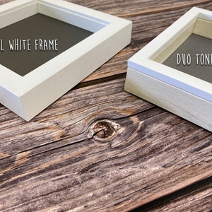 May include: Two picture frames, one white and one with a white border and a natural wood finish. The white frame says "ALL WHITE FRAME" and the other says "DUO TONE FRAME".