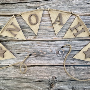 May include: A wooden banner with the name "NOAH" spelled out in individual wooden letters. The banner is strung with twine and has two wooden stars at the ends.