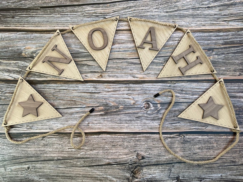 May include: A wooden banner with the name "NOAH" spelled out in individual wooden letters. The banner is strung with twine and has two wooden stars at the ends.