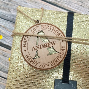 May include: A wooden gift tag with the text "Happy 40th Birthday" and the letter "A" cut out. The name "Andrew" is written below the letter.