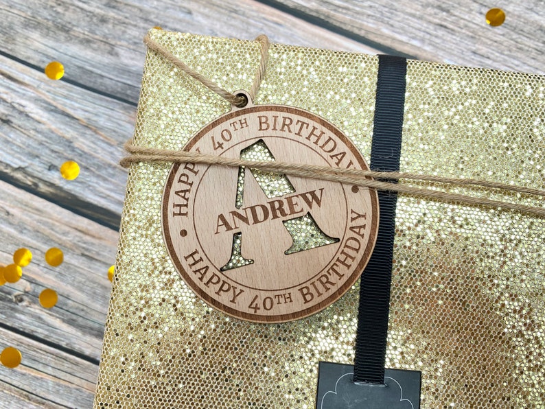 May include: A wooden gift tag with the text "Happy 40th Birthday" and the letter "A" cut out. The name "Andrew" is written below the letter.