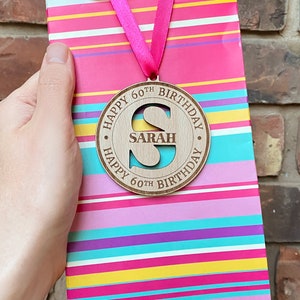 A round wooden tag with a cut-out letter "S" and the text "Happy 60th Birthday Sarah Happy 60th Birthday".