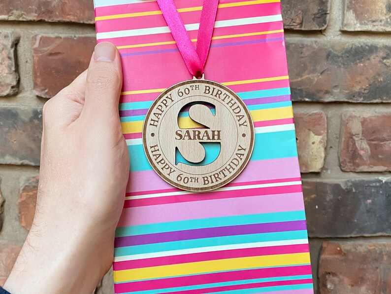 A round wooden tag with a cut-out letter "S" and the text "Happy 60th Birthday Sarah Happy 60th Birthday".