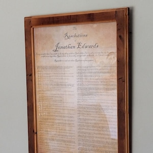 May include: A framed print of "The Resolutions of Jonathan Edwards" in a rustic wooden frame. The print is on aged paper with a brown background and black text. The text includes a quote from Edwards: "I resolve that I am unable to do anything without God's help. I do humbly entreat him by his grace to keep these Resolutions, so far as they are agreeable to his will. For Christ's sake."