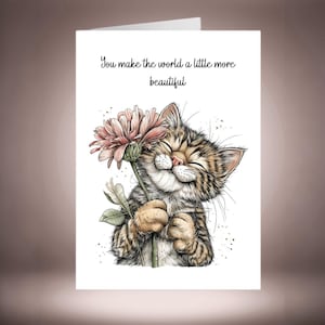 Puede incluir: Tarjeta de felicitación blanca con un gato atigrado sonriente sosteniendo una flor rosa. La tarjeta tiene el texto "You make the world a little more beautiful". El gato es marrón, beige y blanco.