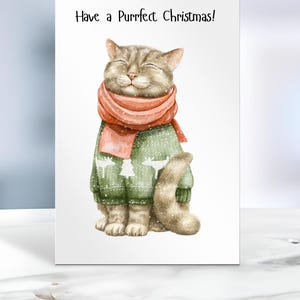 May include: A Christmas card featuring a watercolor illustration of a cat wearing a green sweater and a red scarf. The cat has its eyes closed and is smiling. The card reads "Have a Purrfect Christmas!"