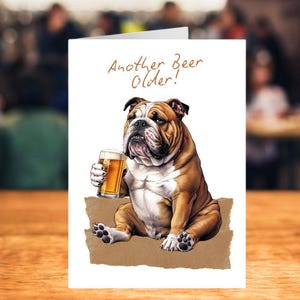 A5 white card with AI image of a bulldog sitting on a brown cushion holding a pint of beer.  Wording at top says "Another Beer Older!"