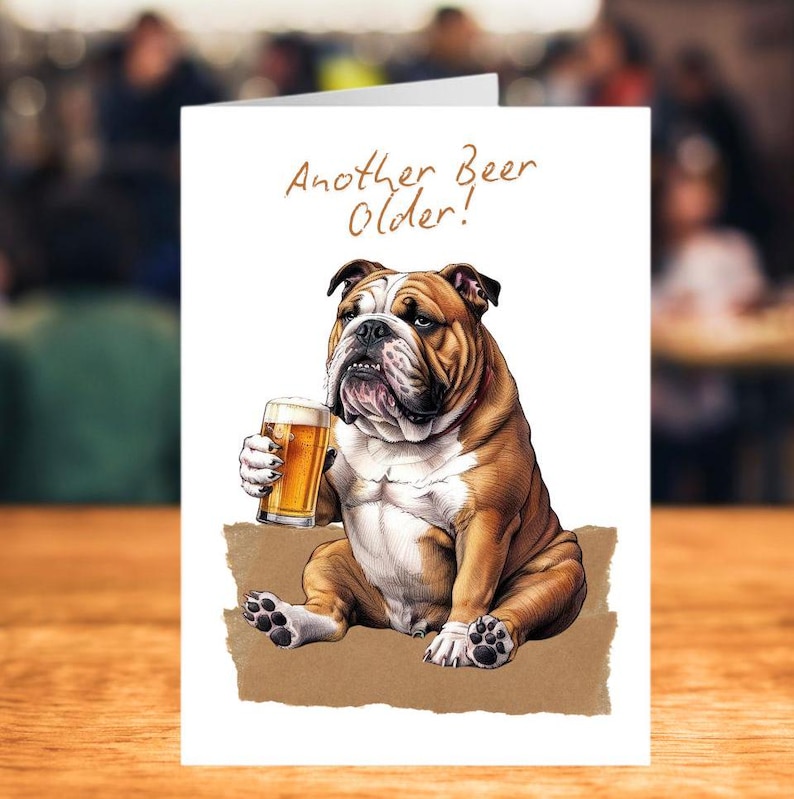 A5 white card with AI image of a bulldog sitting on a brown cushion holding a pint of beer.  Wording at top says "Another Beer Older!"