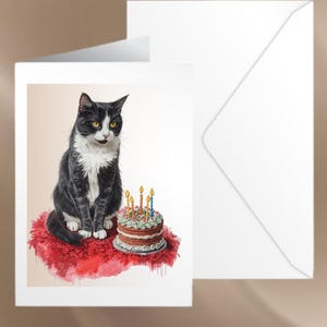 May include: A greeting card featuring a black and white cat sitting on a red cushion next to a birthday cake with lit candles. A white envelope is behind the card. The cat has yellow eyes and is looking at the cake.