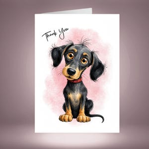 May include: A greeting card featuring a cartoon illustration of a black and tan dachshund puppy with large brown eyes and a red collar. The puppy is sitting against a soft pink watercolor background with the handwritten text Thank You above.