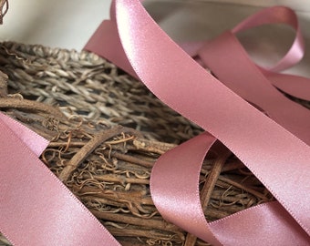 May include: A close-up of a pink satin ribbon. The ribbon is folded and arranged on a woven basket.