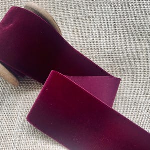 May include: A spool of deep burgundy velvet ribbon. The ribbon is wound around a wooden spool.