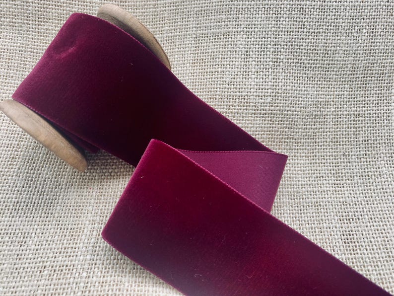 May include: A spool of deep burgundy velvet ribbon. The ribbon is wound around a wooden spool.