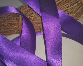 May include: Purple satin ribbon with a shimmery finish. The ribbon is folded and arranged on a brown woven surface.