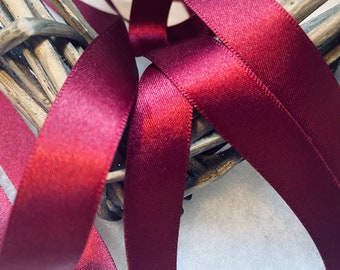 May include: Close-up of a burgundy satin ribbon, woven through a natural wicker wreath. The ribbon is shiny and has a smooth texture.