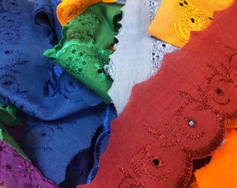 May include: Close-up of colourful embroidered fabric scraps. The image features various colours, including blue, red, green, orange, and purple. The fabric has a scalloped edge and intricate floral embroidery.