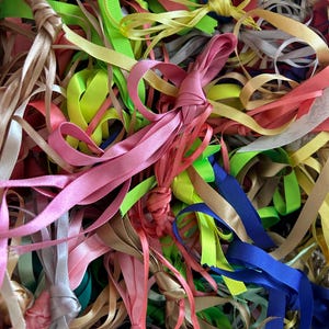 以下が含まれることがあります： ピンク、グリーン、ブルー、イエロー、ベージュなど、さまざまな色合いのリボンが大量に積み重ねられています。リボンはサテン製で、ランダムなパターンで配置されています。