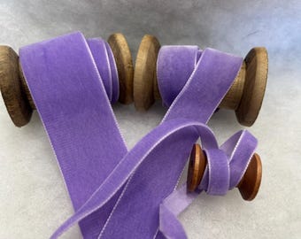 May include: Two spools of lavender purple velvet ribbon with white edges. The ribbon is wrapped around wooden spools.