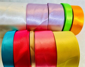 May include: Assortment of satin ribbon rolls in various colors, including white, lavender, lime green, orange, teal, red, gold, and pink.
