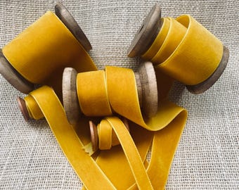 May include: Spools of bright yellow velvet ribbon, wound around wooden spools. The ribbon is arranged in a decorative pattern on a burlap background.