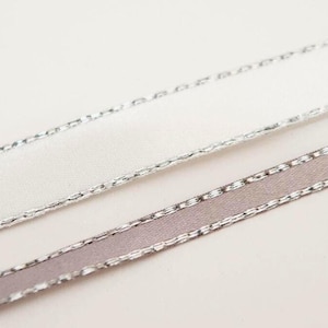 May include: Two rolls of ribbon with silver edges. One roll is white and the other is a light grey.