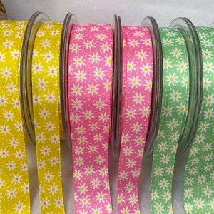 May include: Four spools of ribbon with a white daisy pattern on a yellow, pink, green, and light green background.