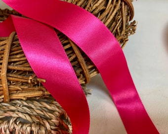 May include: A close-up of a bright pink satin ribbon wrapped around a woven wreath. The ribbon is smooth and shiny, and the wreath is made of natural twigs.