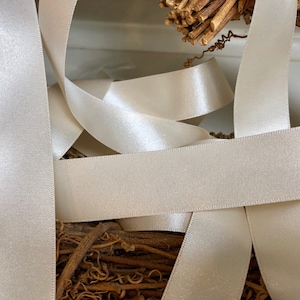 May include: A close-up of ivory satin ribbon, woven together in a criss-cross pattern. The ribbon is soft and smooth, with a subtle sheen.