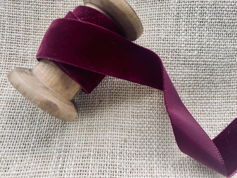 May include: A spool of deep burgundy velvet ribbon. The ribbon is wound around a wooden spool and is ready to be used for crafting or decorating.