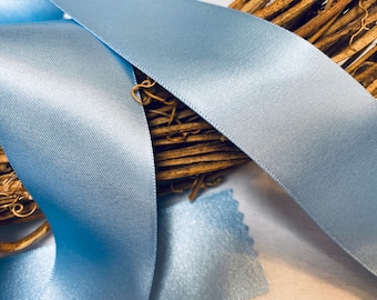 May include: A close-up of light blue satin ribbon. The ribbon is folded and draped over a brown wicker wreath.